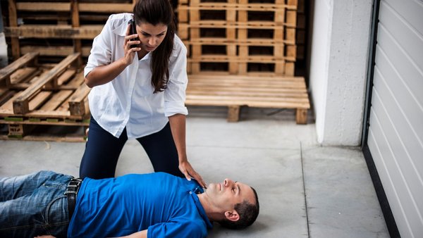 Ein Mann liegt leblos am Boden. Eine Frau hockt daneben und hält ein Telefon an ihr Ohr.