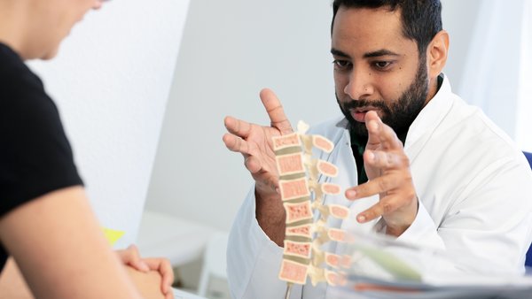 Mohamed Mahde erklärt einer Patientin etwas anhand eines Modells der Wirbelsäule.