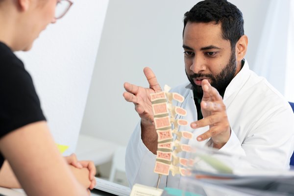 Mohamed Mahde erklärt einer Patientin etwas anhand eines Modells der Wirbelsäule.