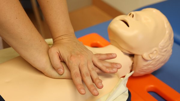 Eine Frau drückt mit beiden Händen auf den Brustkorb einer Dummy-Puppe.